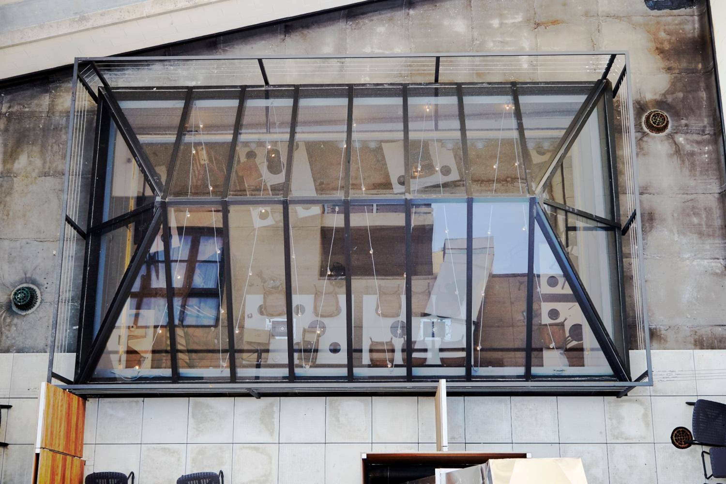 Glass-walled meeting spaces float like transparent boxes above the lobby's weathered concrete floors, where industrial minimalism meets sophisticated transparency in this striking overhead perspective.