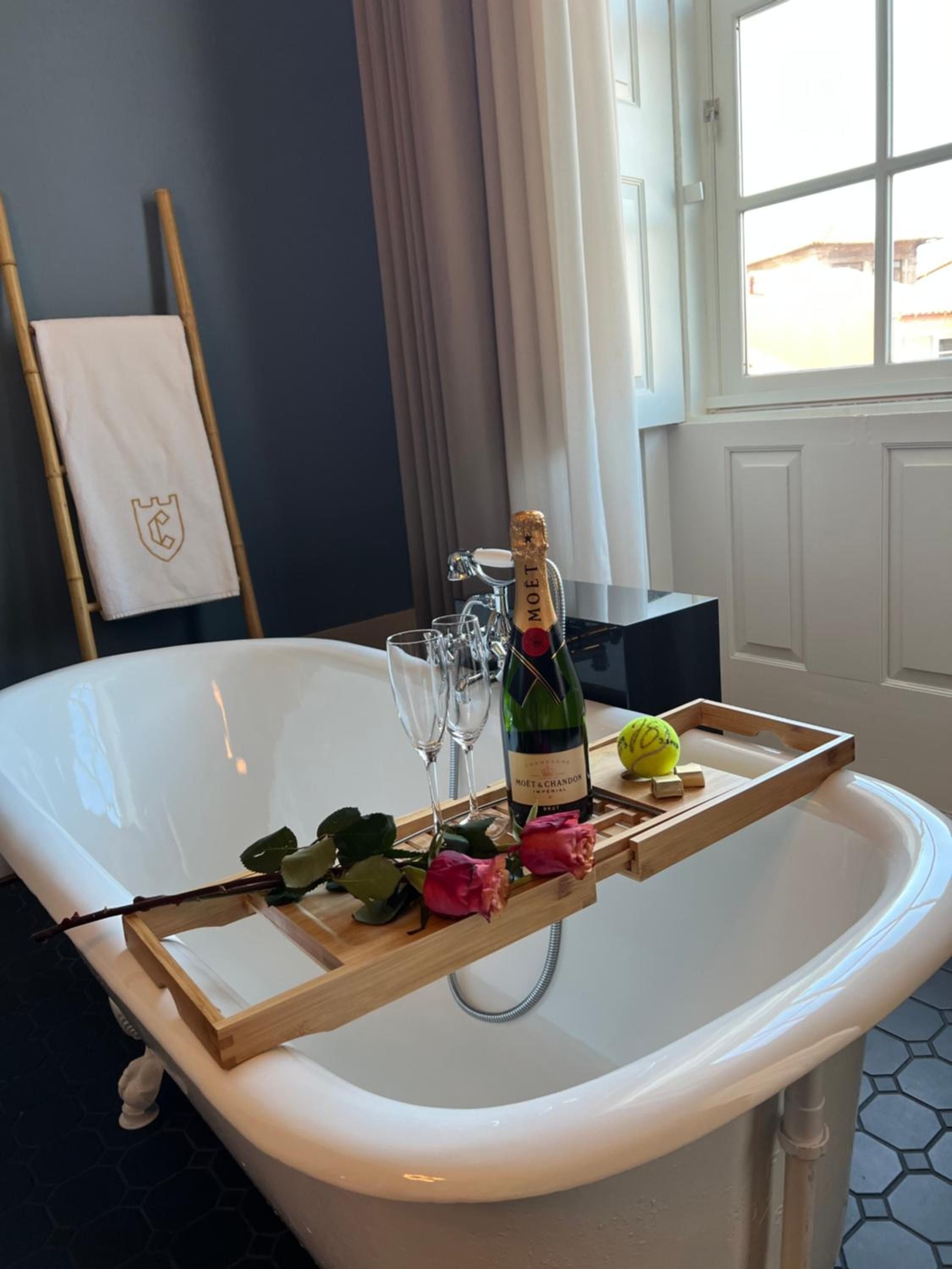 Champagne flutes catch afternoon light on a bamboo bath caddy, where Moët & Chandon and pink roses transform an elegant freestanding tub into pure indulgence.