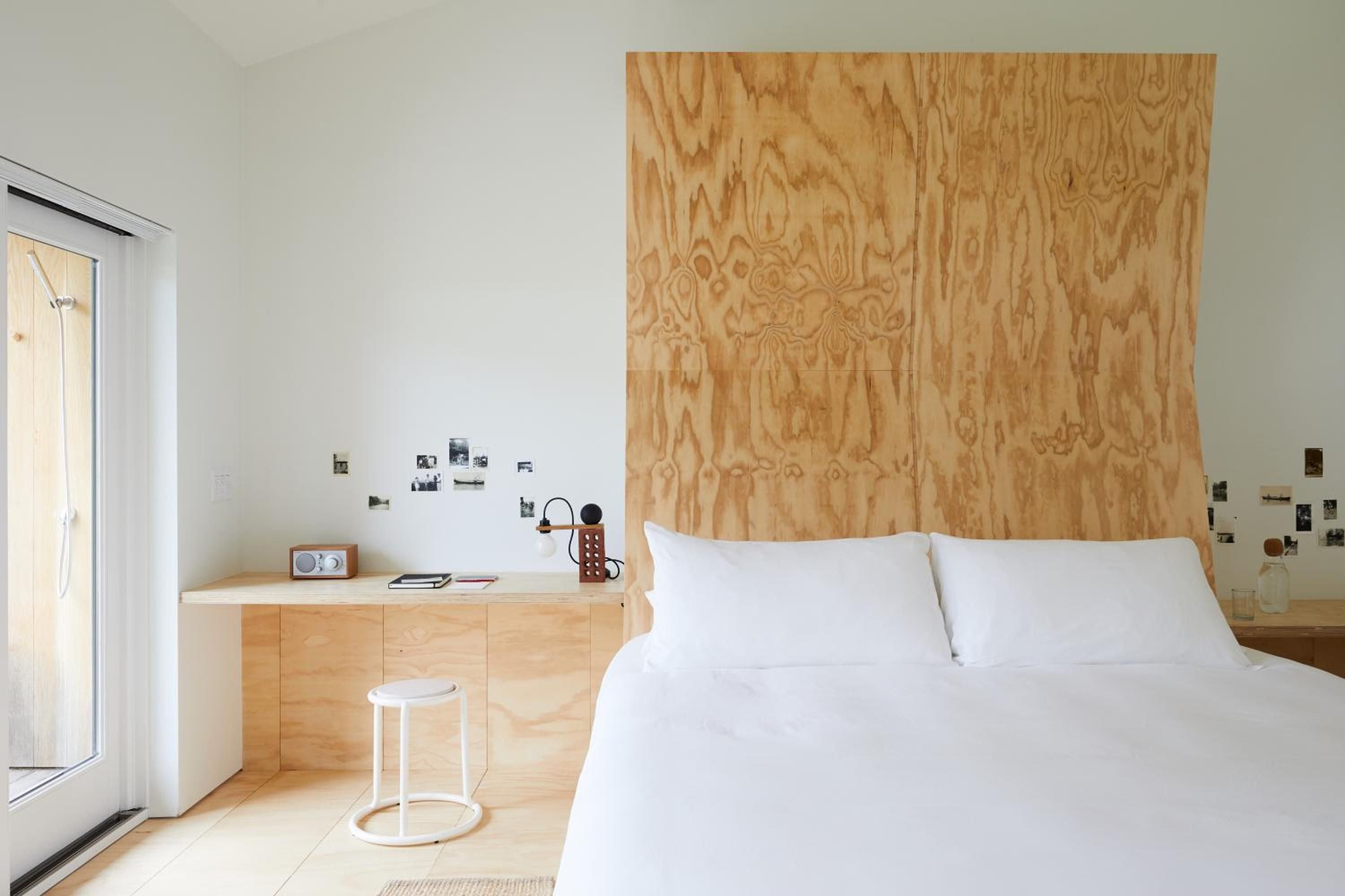 Plywood's warm grain creates an unexpected headboard backdrop, while scattered photos and a vintage radio hint at stories unfolding in this thoughtfully minimal sanctuary.
