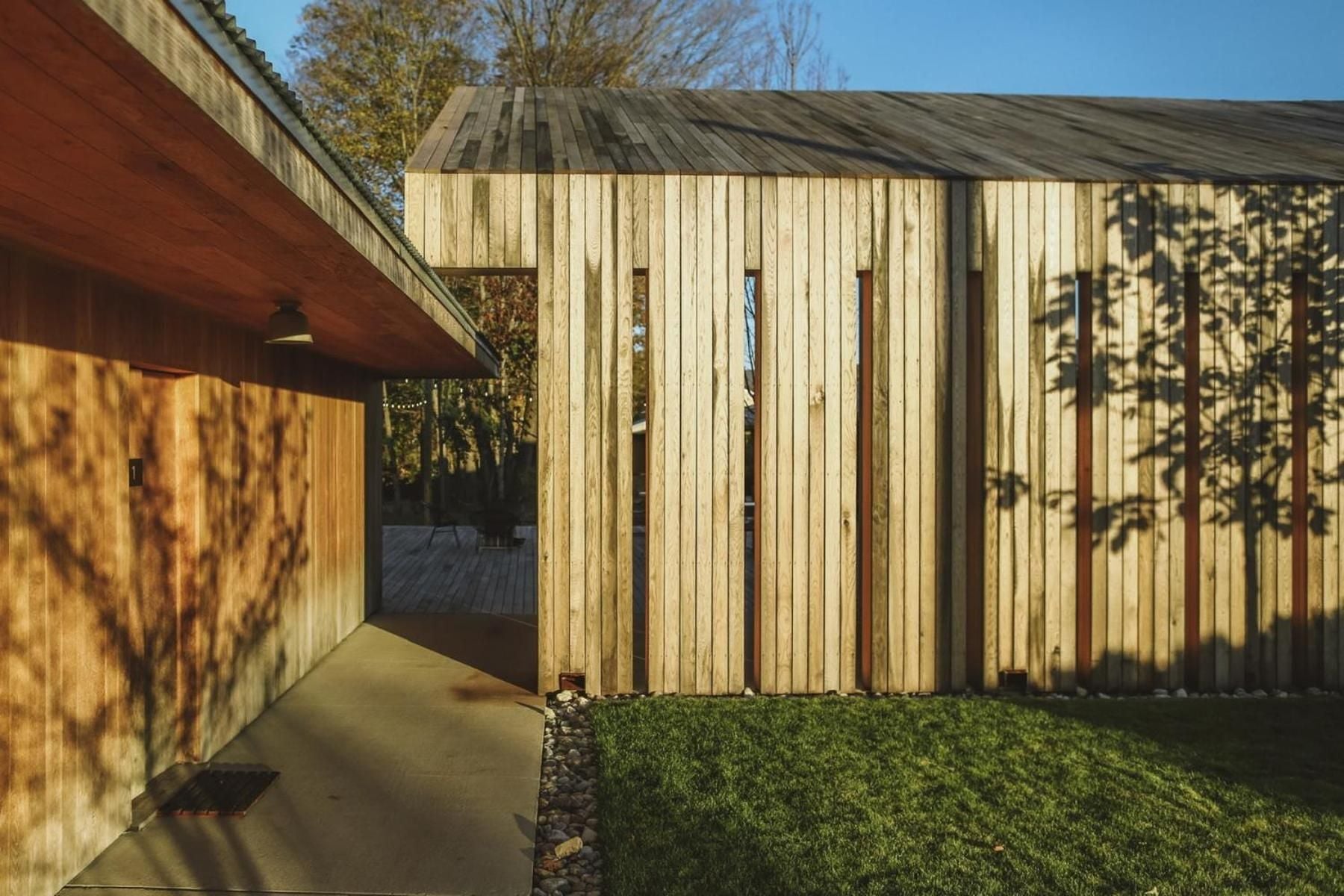 Natural timber cladding catches afternoon light, creating dramatic shadows that dance across the minimalist facade and perfectly manicured lawn below.