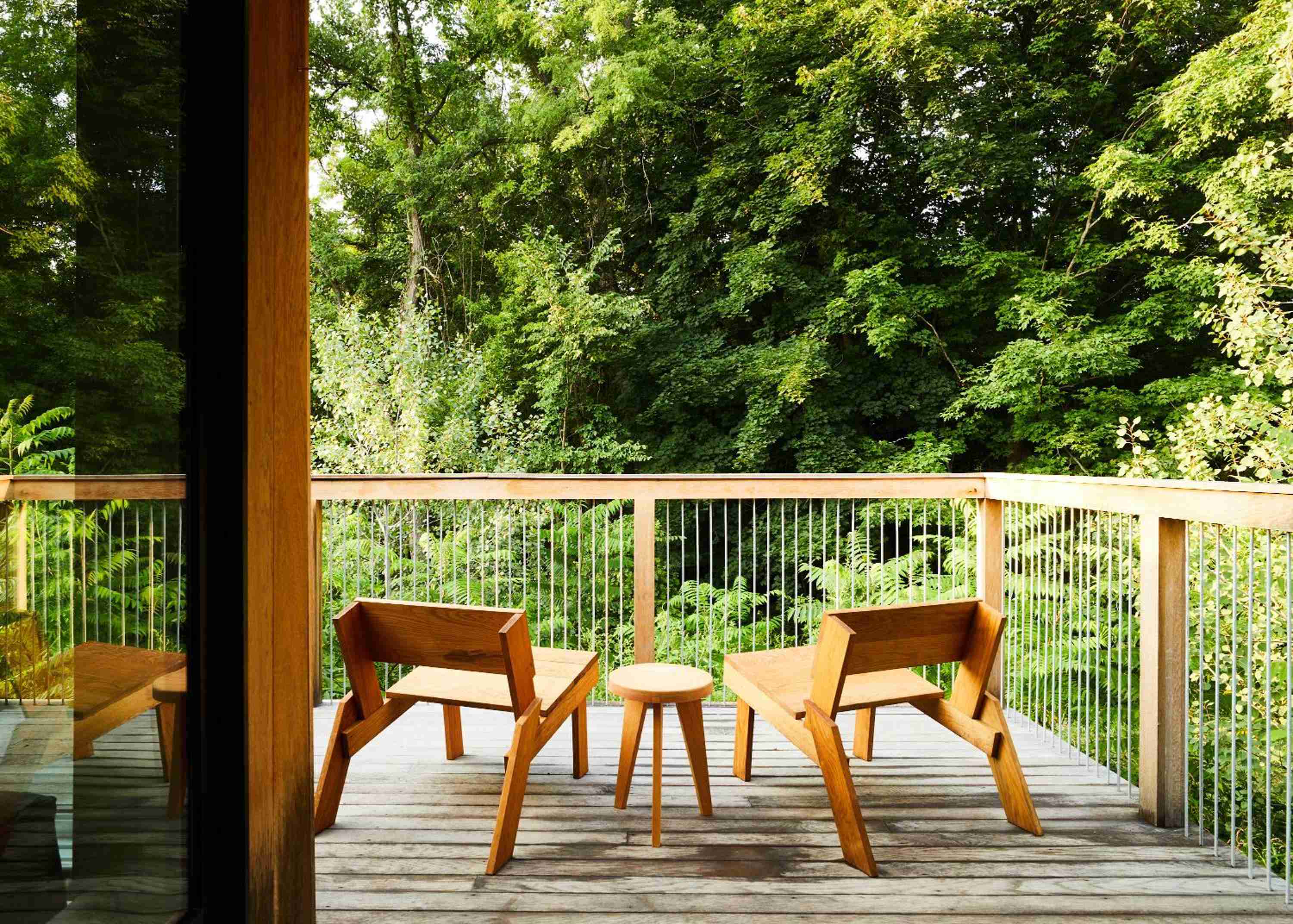 Scandinavian-inspired wooden chairs frame intimate conversations on this forest-facing deck, where vertical railings dissolve into emerald canopy beyond.