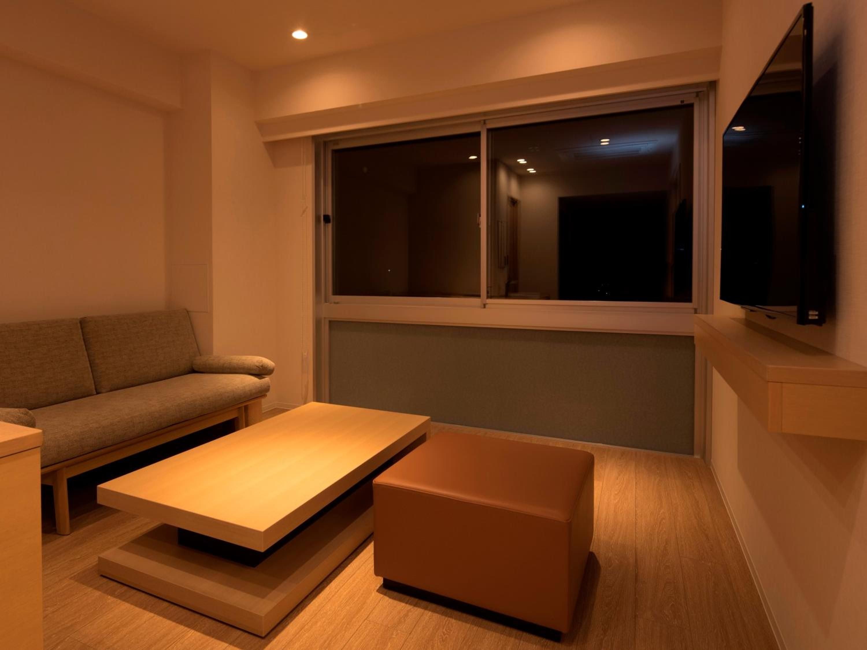 Warm wood tones and clean lines define this minimalist living space, where geometric coffee tables anchor a serene corner bathed in golden evening light.
