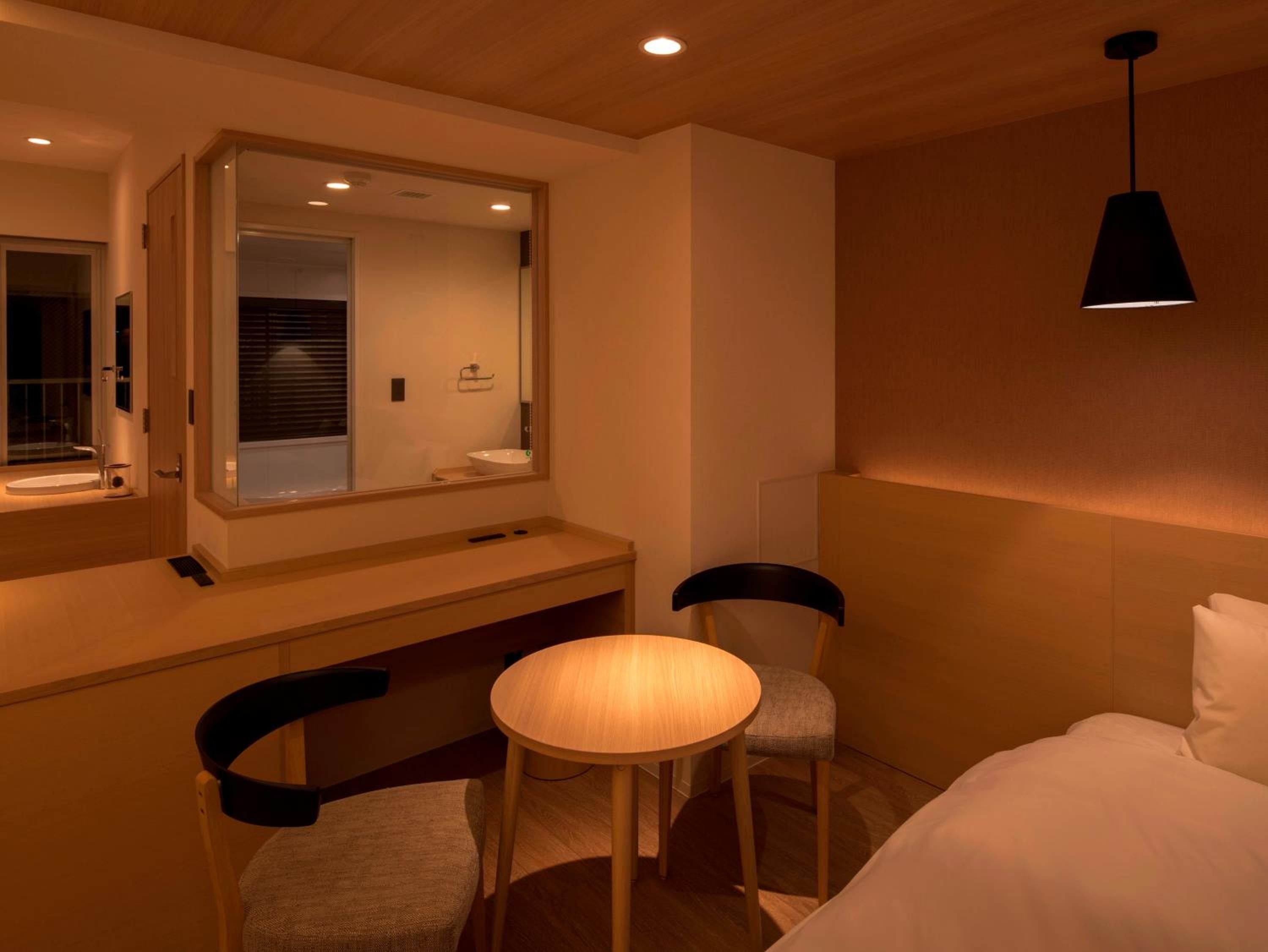 Warm wood tones and soft ambient lighting create an intimate sanctuary, where a curved banquette and round table invite quiet conversation beside the sleek bathroom's glass partition.