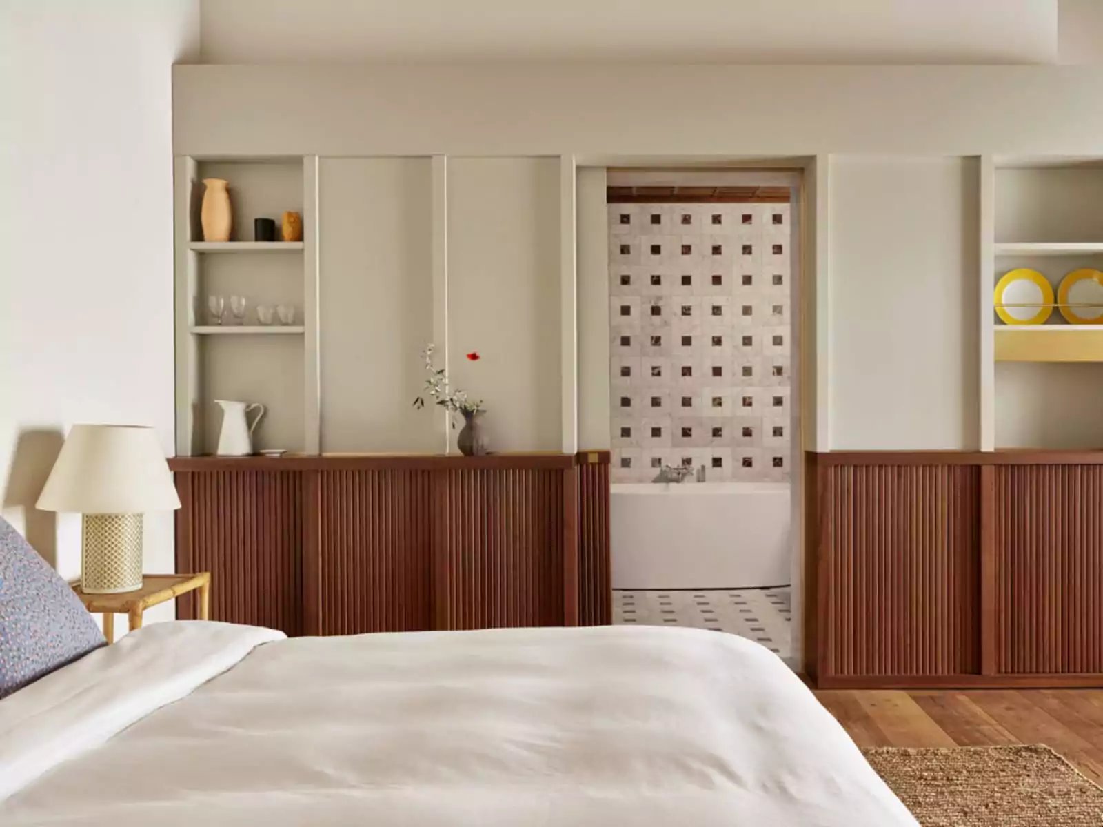 Warm wood paneling meets crisp white shelving in thoughtfully designed suites, where handcrafted details and curated ceramics create an atmosphere of refined Tuscan sophistication.