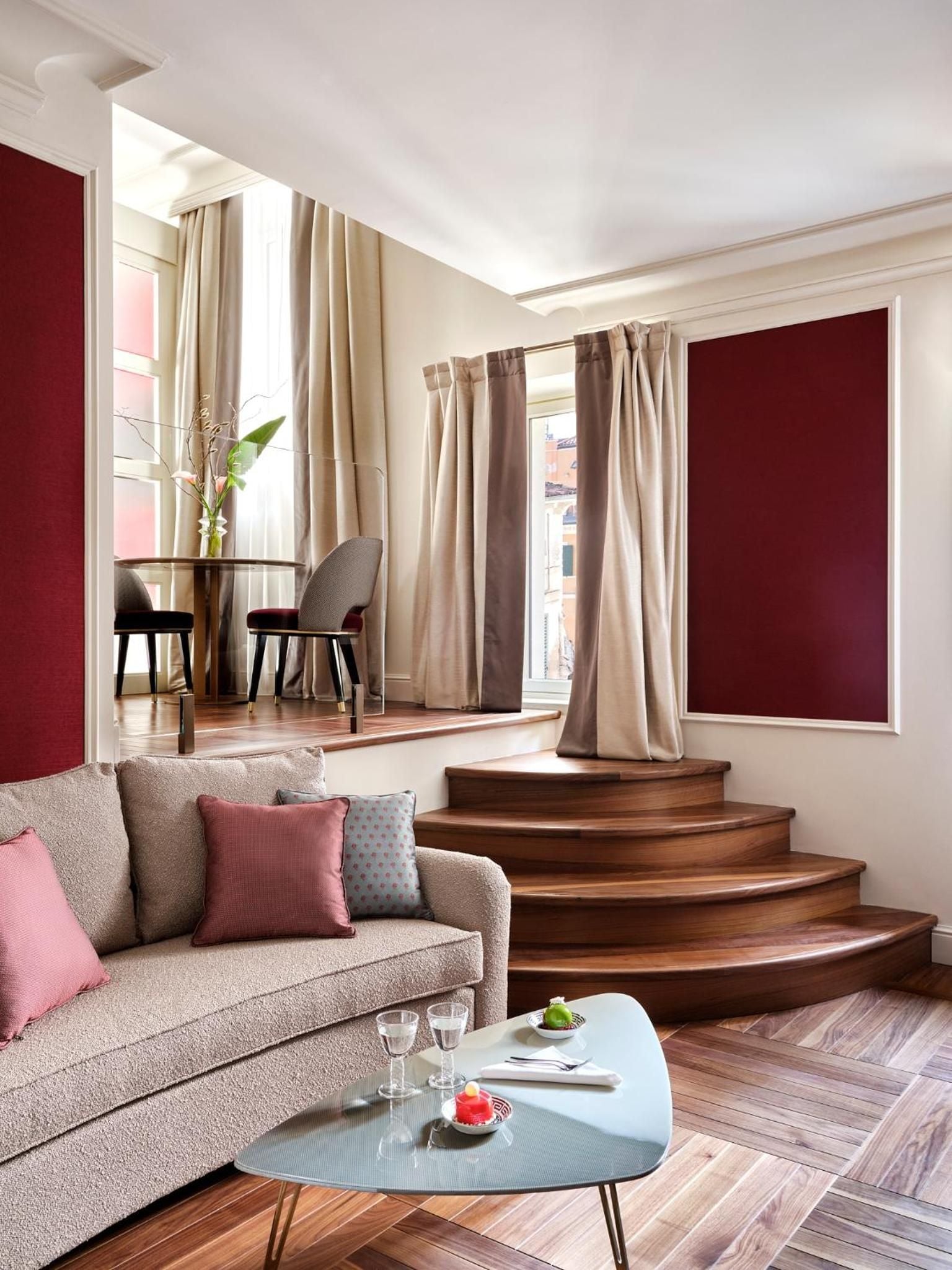 Burgundy accent walls and warm wood steps create intimate drama in this split-level suite, where neutral furnishings and natural light balance bold architectural choices.