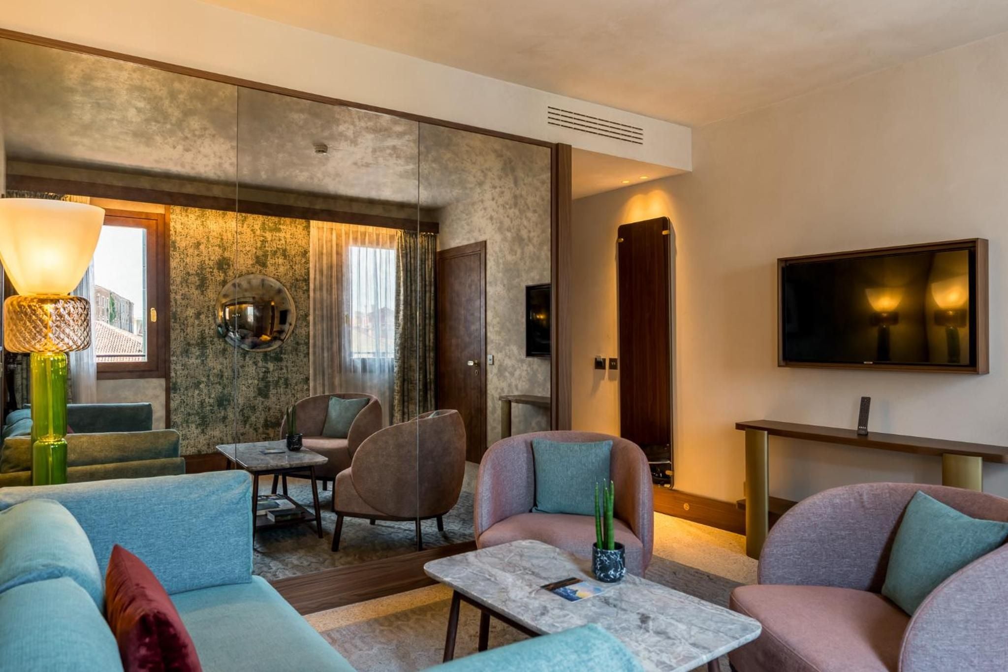 Venetian elegance meets contemporary comfort in the intimate lounge, where jewel-toned furnishings and warm amber lighting create an inviting sanctuary overlooking the lagoon city.