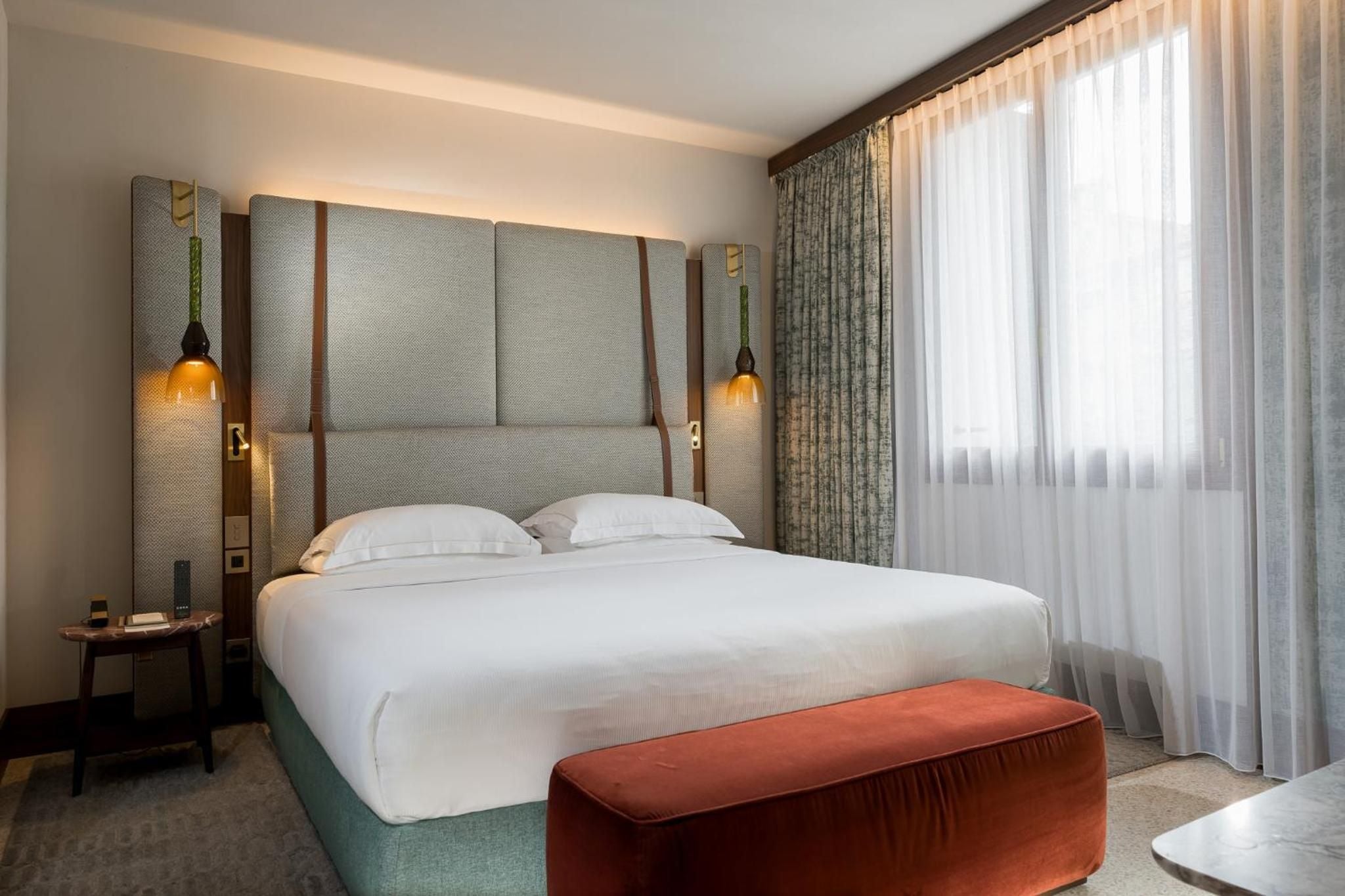Sage-green upholstered headboard and leather straps create sophisticated restraint, while amber pendant lights cast intimate pools of warmth over crisp white linens.