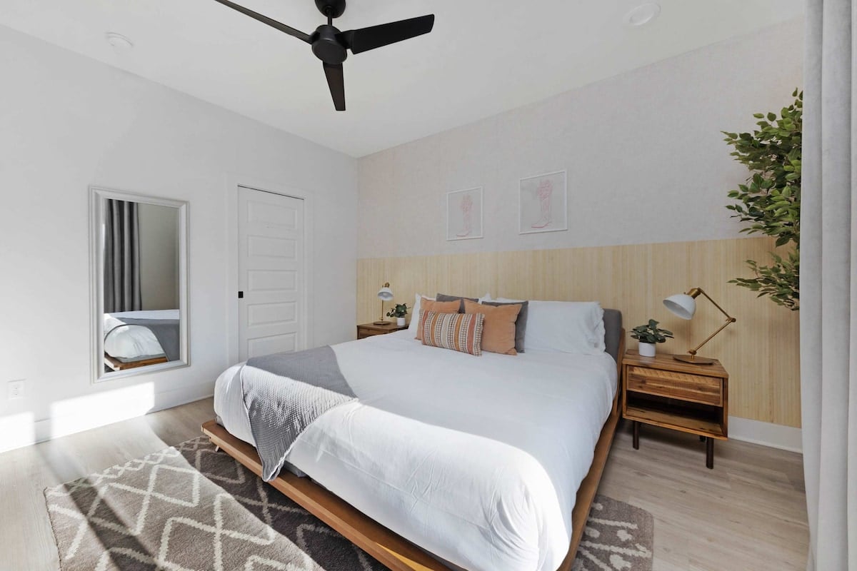 Elegant bedroom featuring a king bed, walk-in closet, and a private balcony with two chairs. Includes an en-suite bathroom with a sleek shower.