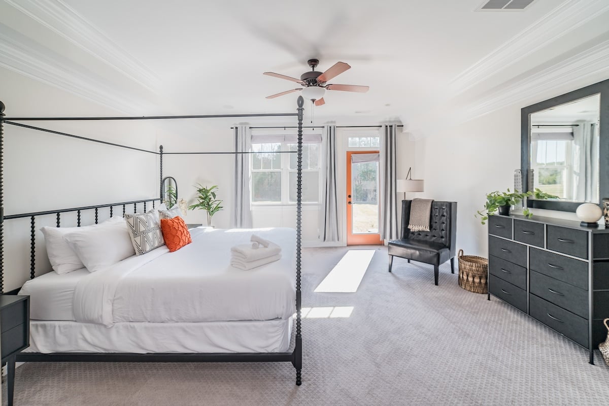 Primary bedroom includes a king bed, dresser, walk in closet, oversized sitting chair, blackout curtains, and primary bathroom.