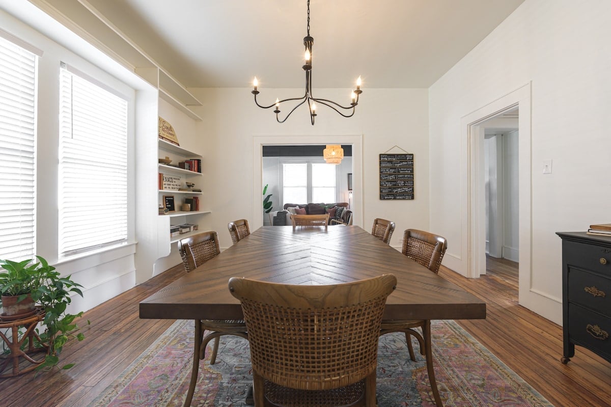 CAPTION: Located in Waco, US, "Property" exudes a blend of rustic charm and modern elegance. The interior showcases a farmhouse-style dining area with a striking wooden table set against light cream walls. Natural light floods through large windows, highlighting a minimalist yet inviting ambiance. Wicker seating and warm wooden floors enhance the cozy atmosphere, while the neutral color palette creates a serene environment ideal for travelers seeking relaxation and comfort.