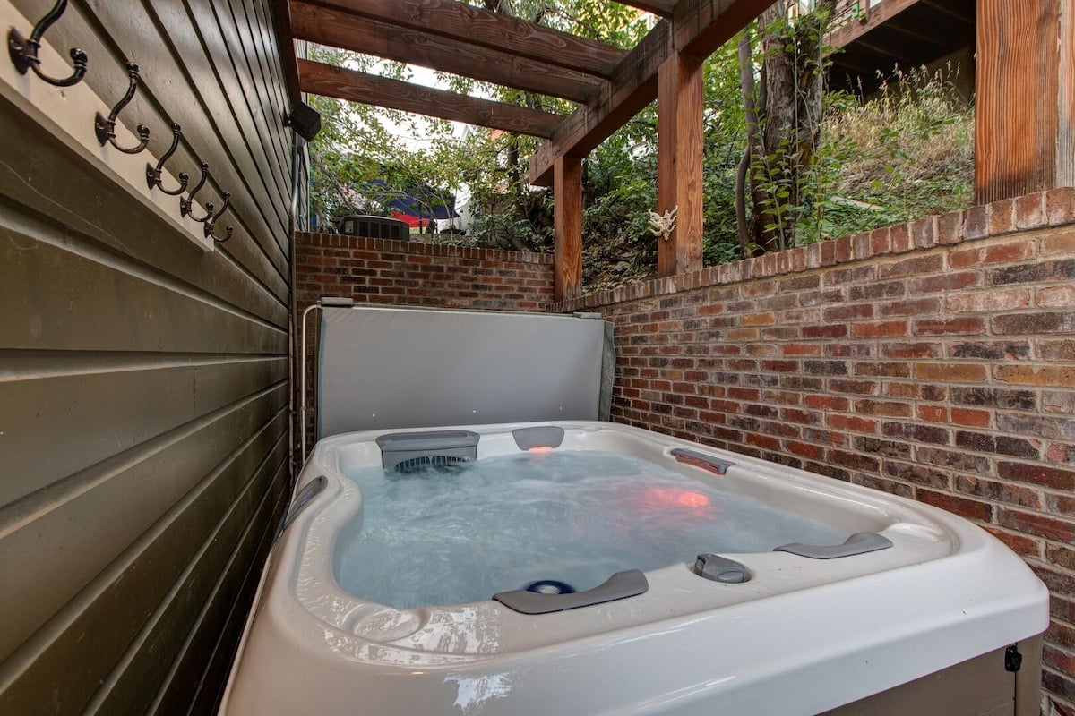 **CAPTION:** Nestled in Park City, "Property" exudes rustic elegance with its alluring hot tub area. Encased by a warm brick wall and natural wood beams, this outdoor feature creates an inviting haven for relaxation. The soothing neutral tones and verdant surroundings enhance the serene atmosphere, making it an ideal retreat for travelers seeking tranquility and luxury. This exquisite architectural blend offers a perfect escape, appealing to those desiring a seamless fusion of nature and comfort.
