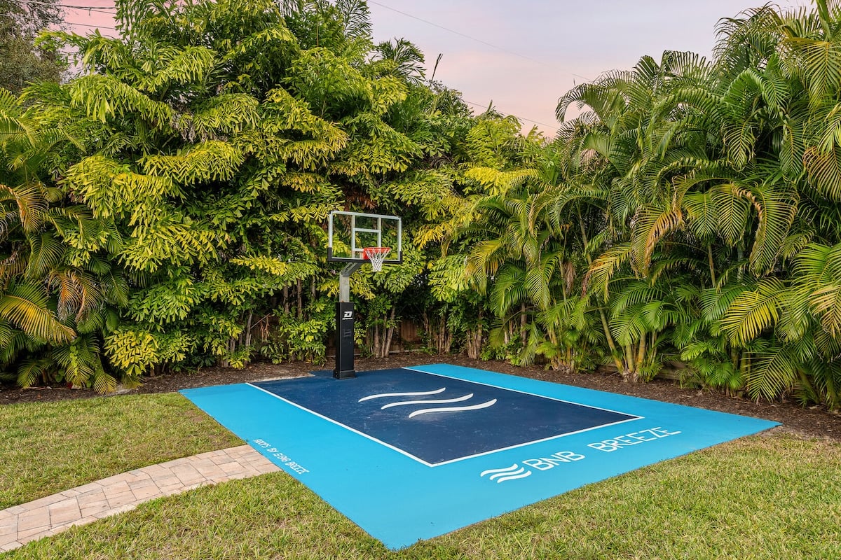 CAPTION:
The "Property" in Sarasota showcases a contemporary outdoor luxury with its private basketball court nestled amidst lush tropical foliage. The vibrant blue and green color palette creates a refreshing contrast, embodying a serene yet invigorating atmosphere. Ideal for sports enthusiasts and relaxation seekers, this unique feature offers a perfect blend of athletic appeal and natural beauty, enticing travelers looking for a luxurious and active retreat.