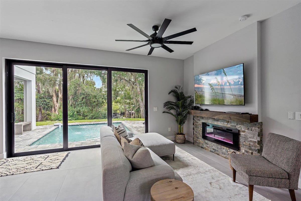 Cozy up in the main living room with pool views, a 65” Smart TV, and a sleek electric fireplace.