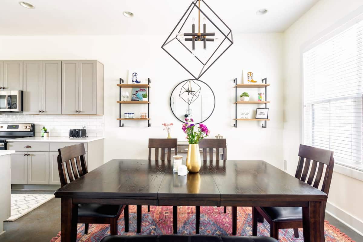 The dining area features a large table that seats 6 guests, complemented by a stylish chandelier.