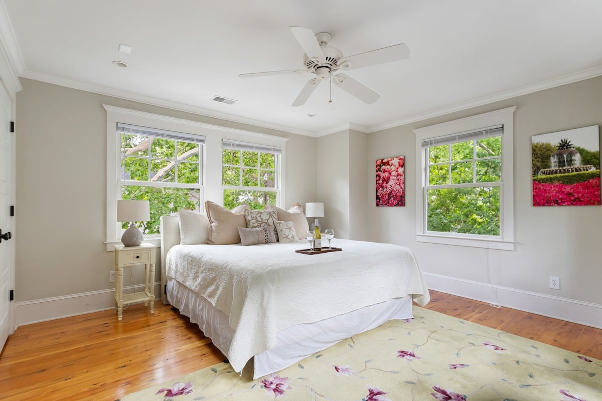CAPTION: Experience the charm of "Property" in Charleston, where Southern elegance meets modern comfort. This inviting bedroom features a serene minimalistic design with soft, neutral tones. The sunlit space is highlighted by polished wooden flooring and lush green views through large windows. Cozy and sophisticated, this room offers travelers a serene retreat, making it ideal for those seeking luxury and tranquility. Perfect for guests seeking an authentic Southern experience.