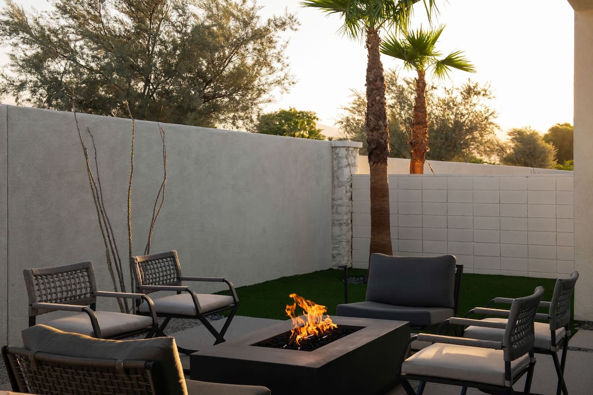 Enjoy a peaceful evening around the outdoor fire pit, surrounded by lush faux grass and palm trees at sunset.