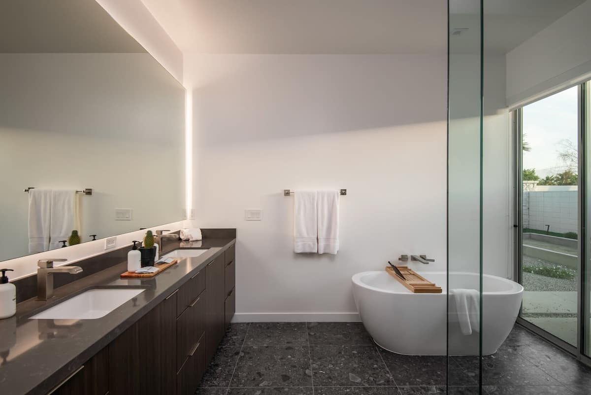 The Primary Bathroom offers a luxurious soaking tub and double vanity with elegant backlit mirrors, overlooking a private garden.
