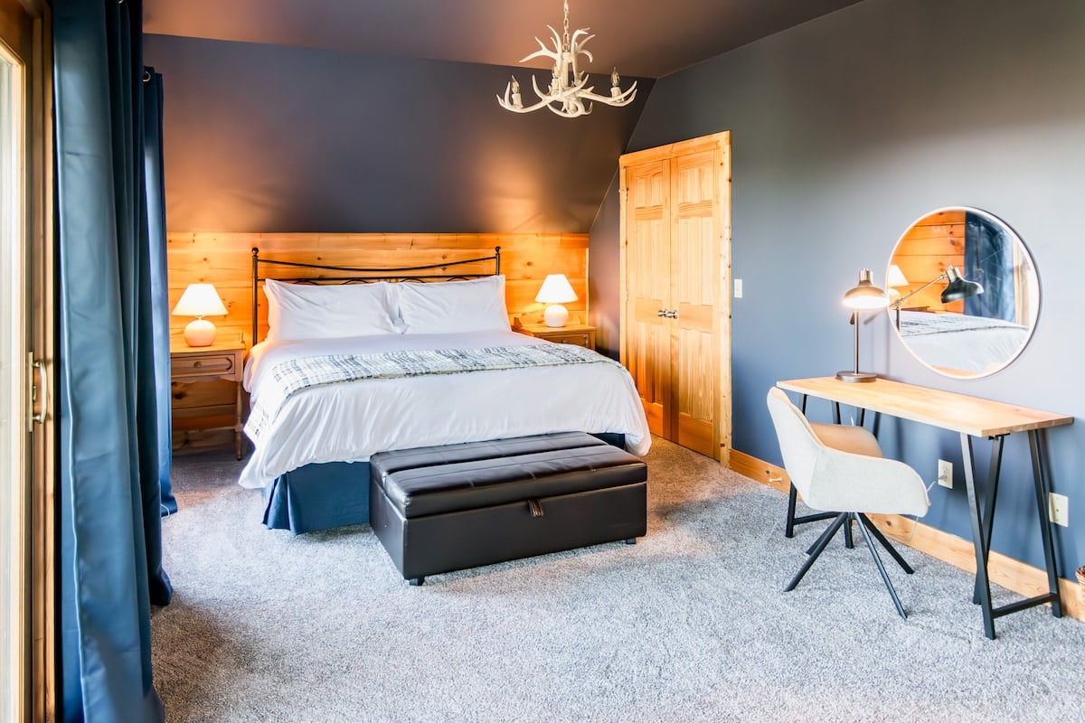 Romantic primary bedroom with king bed, antler chandelier, TV, dresser, desk, twin pullout, and small private deck
