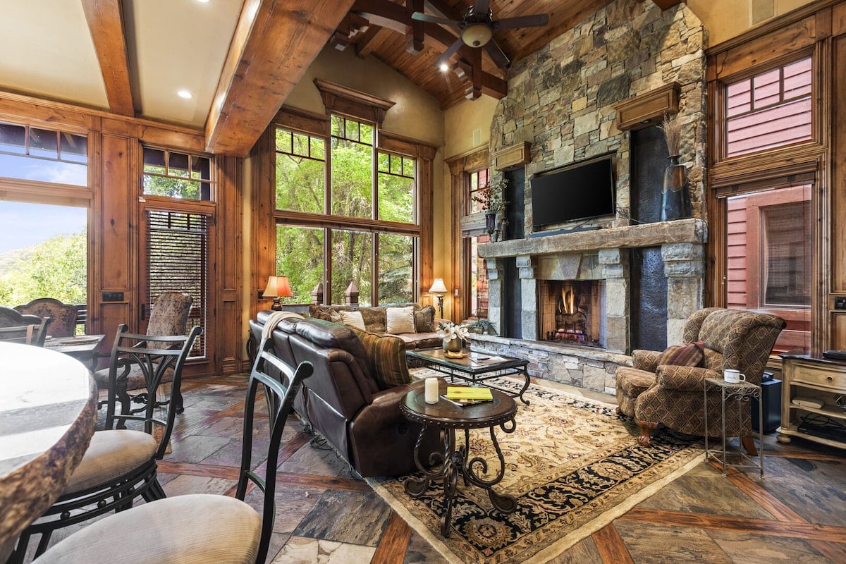 CAPTION: Nestled in the picturesque landscapes of Park City, "Property" showcases a rustic yet elegant architectural style, blending natural wood and stone elements for a cozy atmosphere. The expansive living area features a stone fireplace and large windows that flood the space with natural light, offering stunning views of the outdoors. The earthy color palette of browns and greens enhances the warm, inviting mood, making it ideal for luxury travelers seeking a serene mountain retreat.