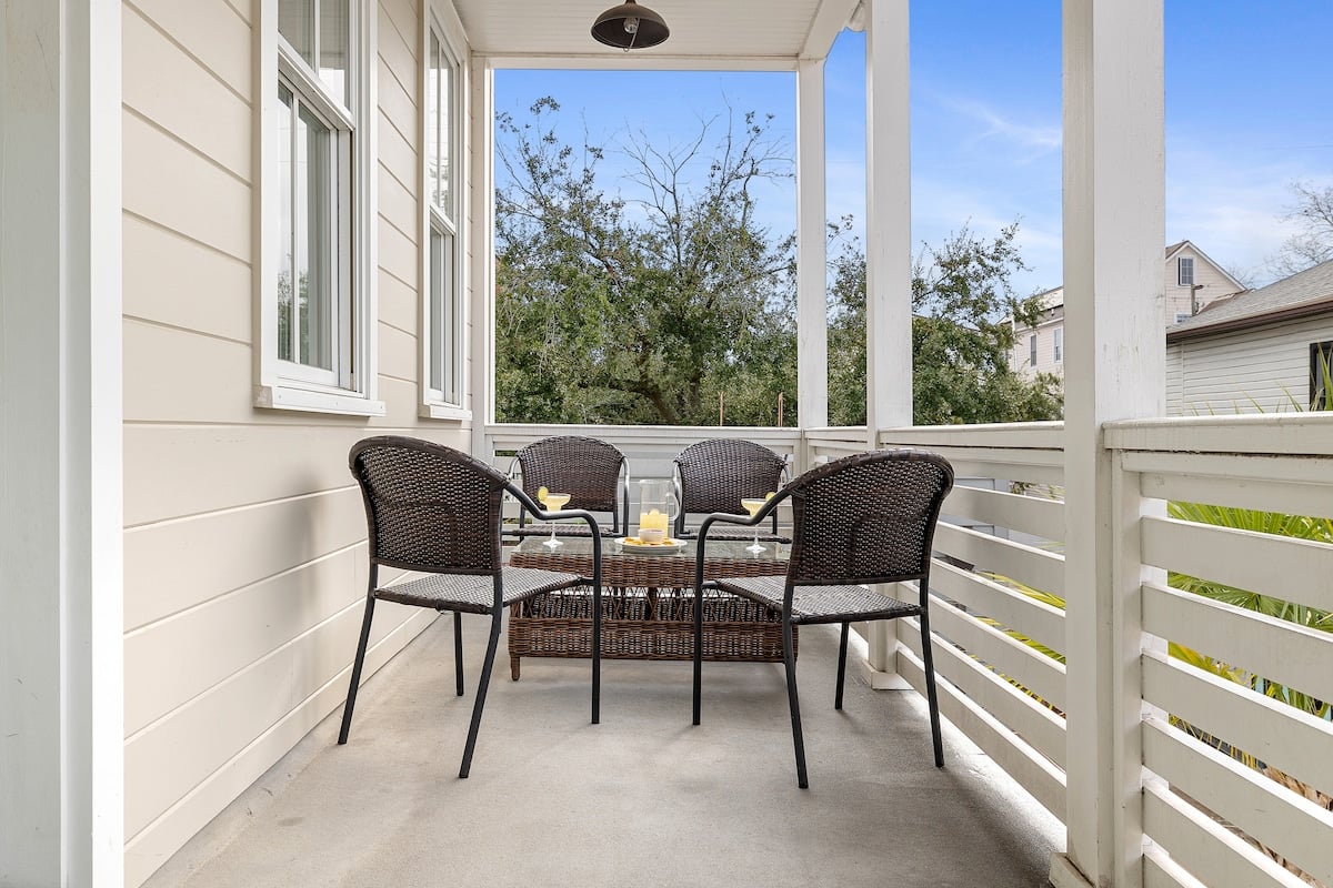 CAPTION: Discover tranquility at "Property," a luxury travel haven in Charleston. This charming architectural gem features a cozy porch setting with elegantly woven chairs and ambient candle accents. Bathed in neutral tones of cream and brown, this outdoor retreat invites relaxation amidst lush greenery. Perfect for travelers seeking a serene escape, the property blends classic Southern charm with modern comforts, offering a picturesque setting for a memorable stay.