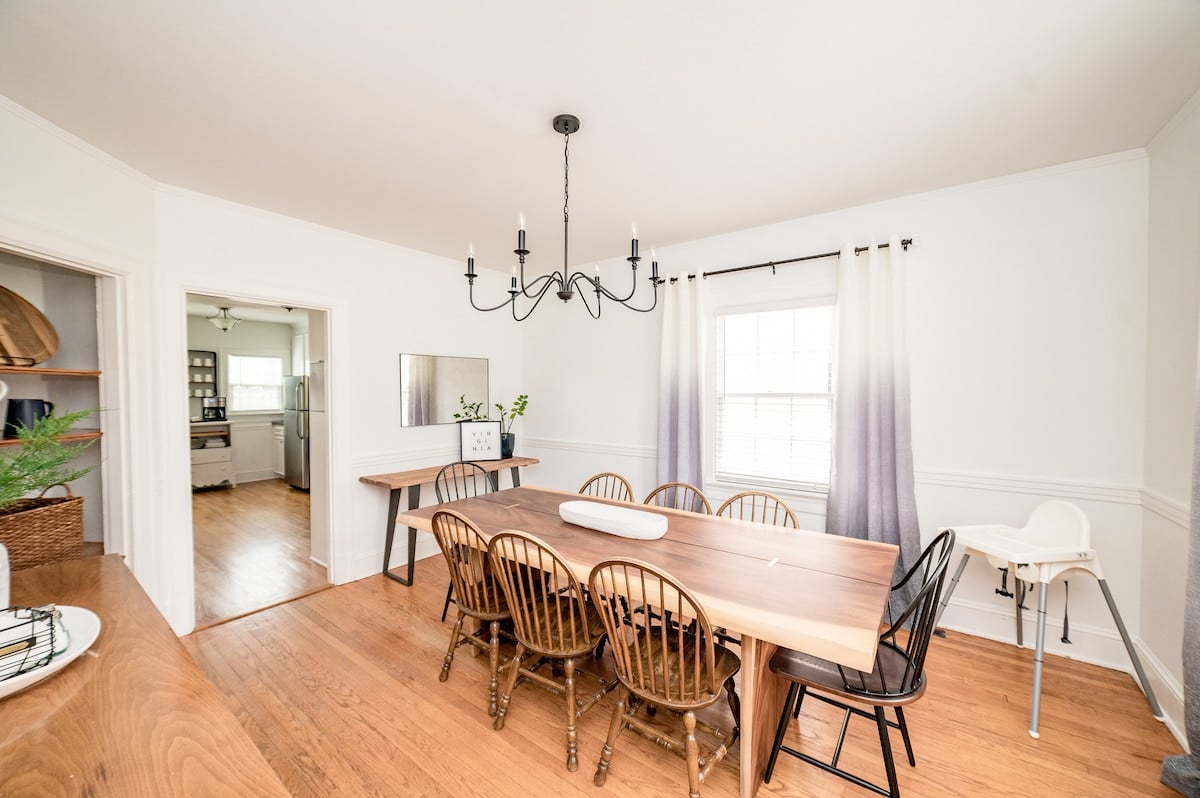 CAPTION: Discover the charm of the "Property" in Lynchburg, US, featuring a modern farmhouse dining room with a serene atmosphere. The space boasts a long, natural wood dining table paired with an eclectic mix of chairs against a clean white backdrop. Elegant, minimalistic chandelier lighting complements the airy ambiance, inviting warm, sunlit gatherings. Perfect for travelers seeking a blend of contemporary comfort and rustic appeal.