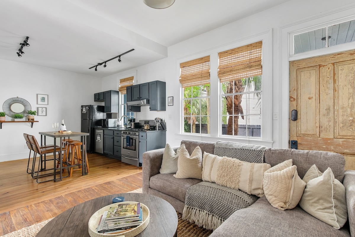 **CAPTION**: Discover "Property" in Charleston, a charming blend of modern and rustic styles. This luxury travel property features an inviting open-plan living area, showcasing a muted color palette with rich wood tones and soft neutrals. The cozy atmosphere, complemented by bamboo window shades and plush furnishings, appeals to travelers seeking a serene and stylish retreat. The sophisticated decor ensures a memorable and relaxing stay amidst Charleston's historic beauty.