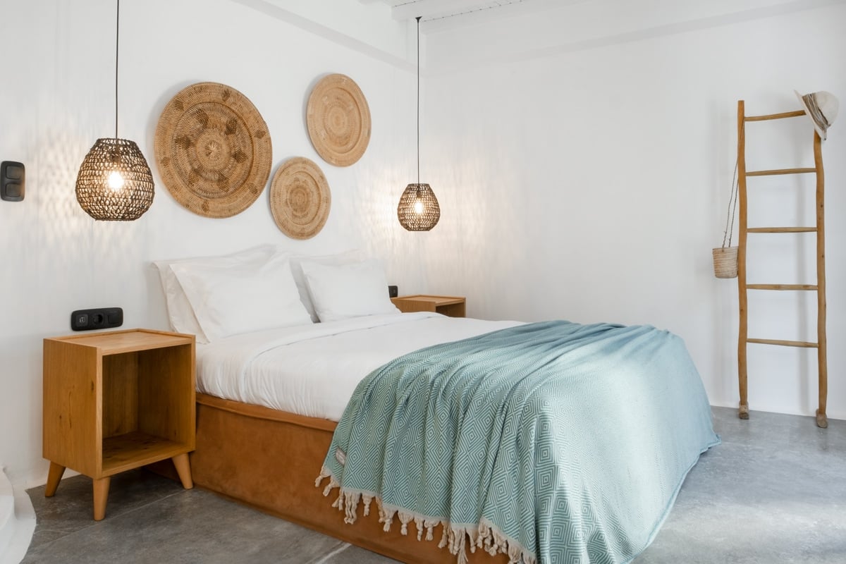 CAPTION: 
"Property in Platis Gialos, GR, epitomizes minimalist luxury with its airy, contemporary design. The neutral palette of whites and beiges is accented by natural wood tones and soft textiles, creating a serene and inviting atmosphere. Key features include textural wall art, modern pendant lighting, and a ladder-style towel rack, adding to the understated elegance. This chic retreat is ideal for travelers seeking tranquility and style amidst the scenic beauty of Greece."