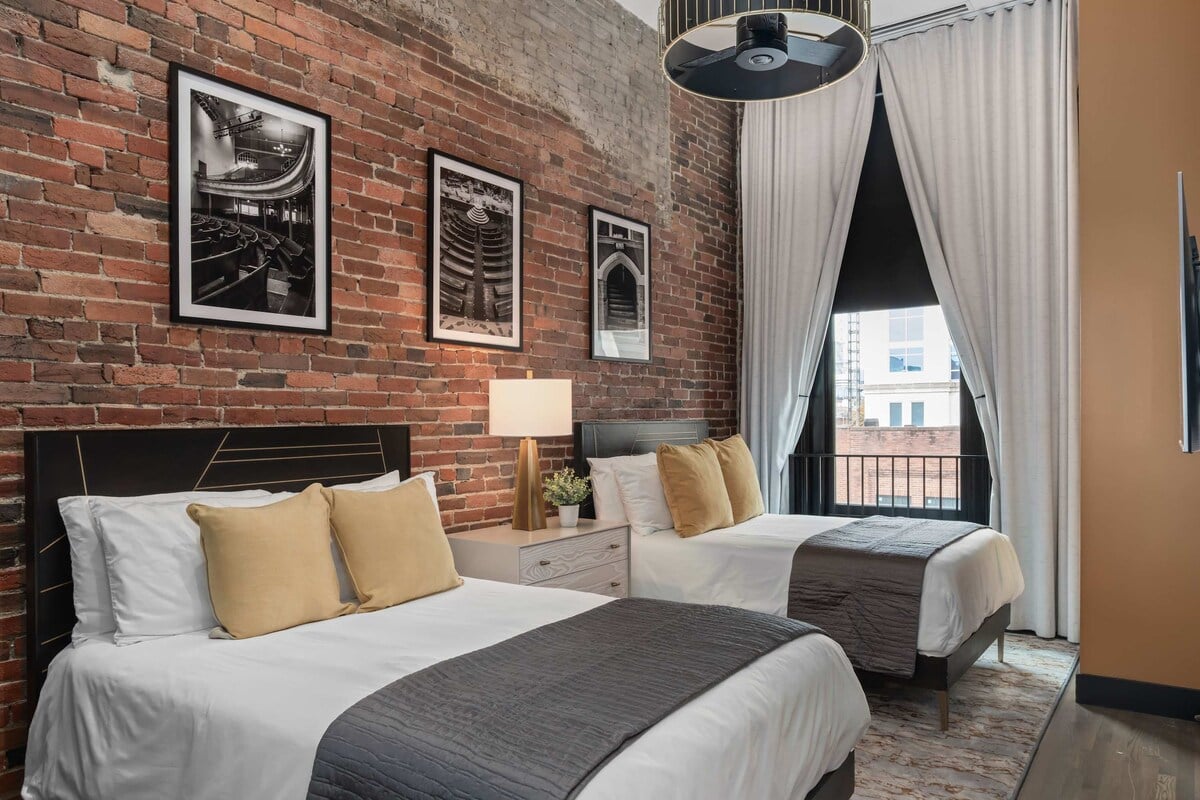 “Inviting double bedroom with exposed brick, tall windows, and warm natural light. Thoughtful design details create a boutique, loft-style stay in the heart of downtown