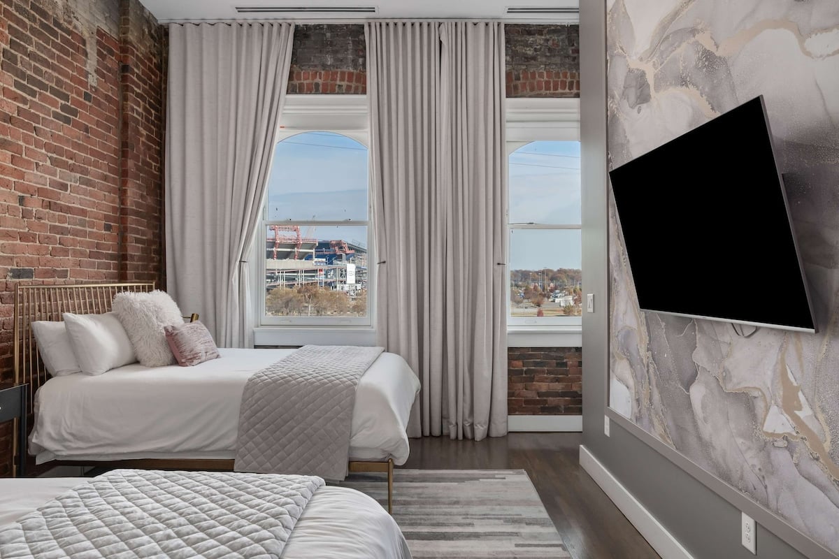 River-view queen bedroom featuring two queen beds, exposed brick, and a wall-mounted smart TV for easy streaming.