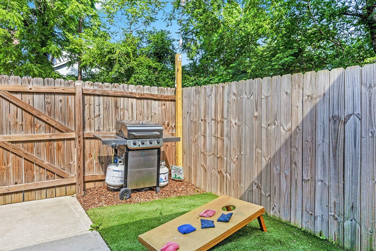 The backyard features a propane grill (propane provided) and a cornhole setup.