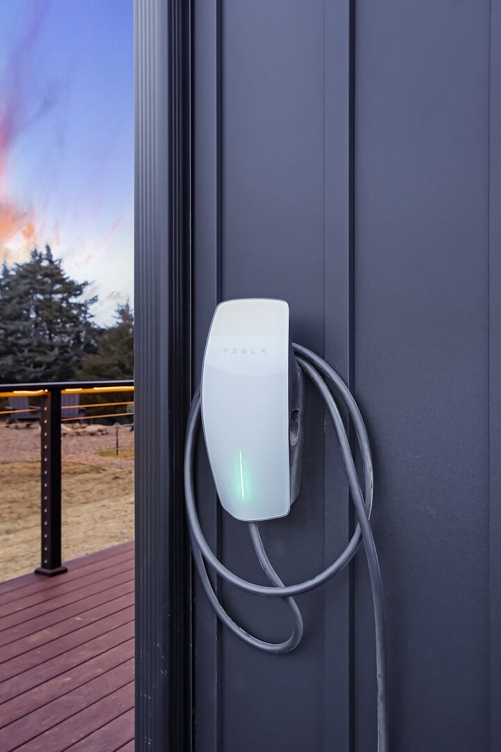 Plug into the Tesla charging port available to you! Located on the side of the home by the entrance.