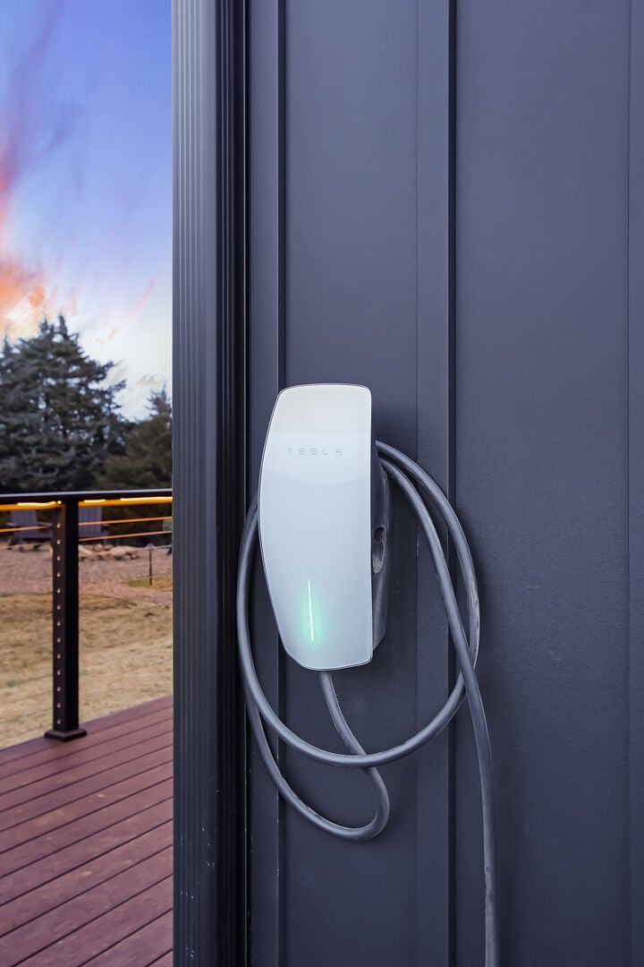 Plug into the Tesla charging port available to you! Located on the side of the home by the entrance.