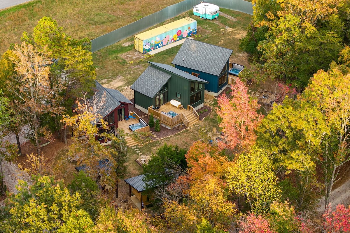 CAPTION: Nestled in the vibrant autumn landscape of Bloomington Springs, "Property" exudes rustic charm with its contemporary architectural style. The cabins are surrounded by a tapestry of colorful foliage, offering a serene and secluded atmosphere. The use of natural wood and earthy tones complements the rich greens and fiery reds of the setting, creating an inviting retreat. Ideal for travelers seeking tranquility alongside nature's beauty, this property promises a rejuvenating escape.