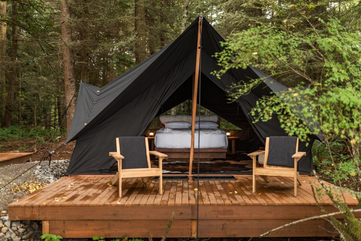 CAPTION: Nestled amidst the serene forests of Port Angeles, "Property" offers a unique luxury glamping experience that combines rustic elegance with modern comfort. The architectural style of the tent features a classic black canvas set against lush greenery, creating a tranquil retreat. The natural wood deck and cozy interior, accented by earth tones, invite travelers seeking a peaceful escape. Perfect for nature lovers and luxury seekers alike.