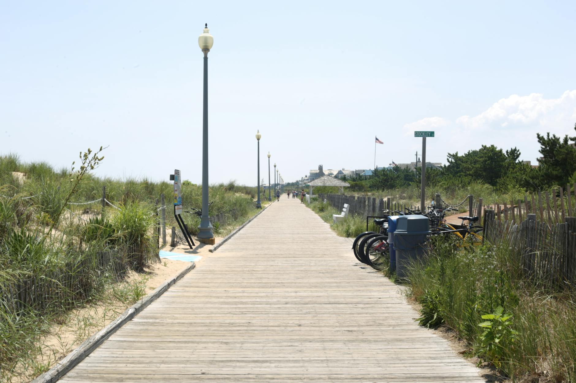 Scenic view of a tranquil beach boardwalk lined with grass and bikes on a sunny day.