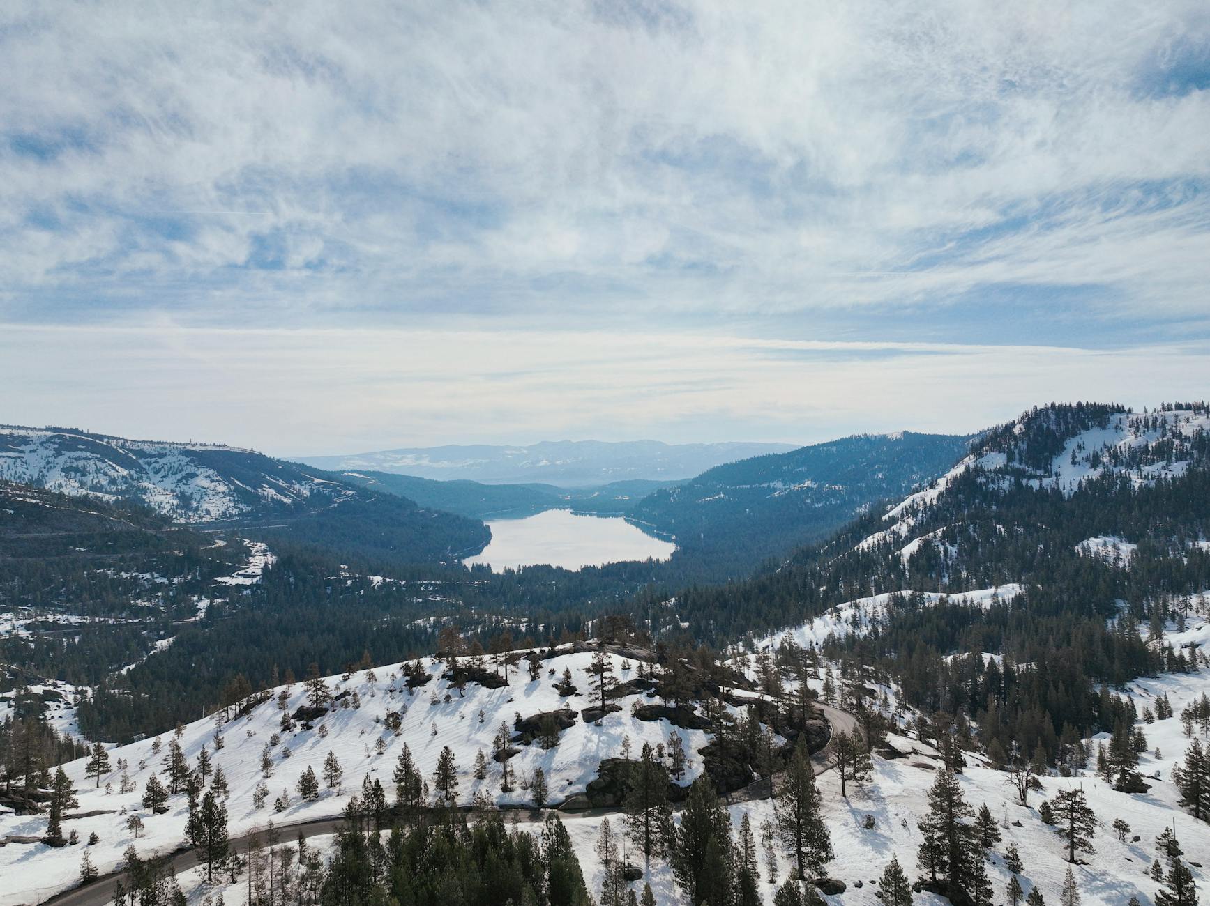 Breathtaking aerial view of Donner Lake surrounded by snow-covered mountains under a cloudy sky.