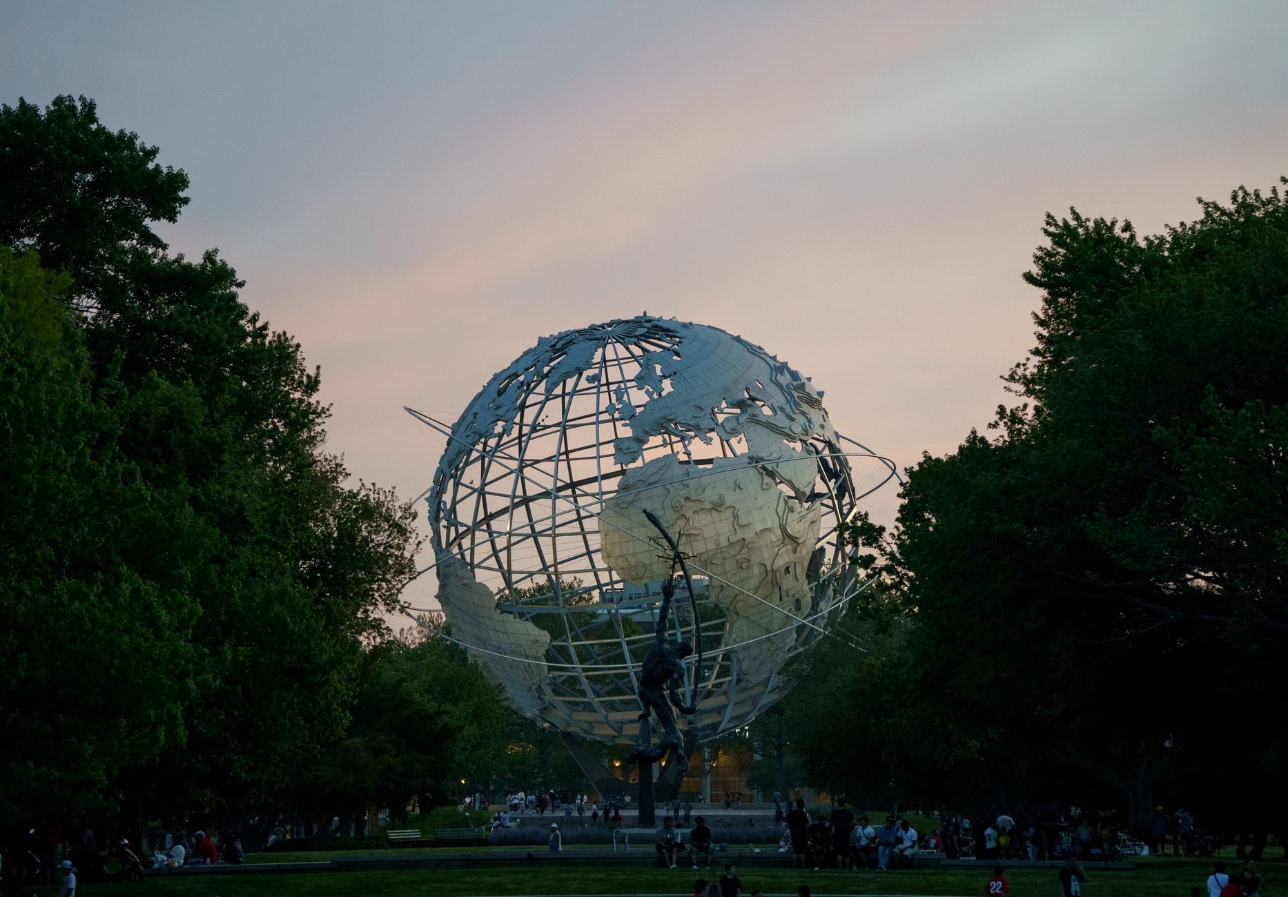 The iconic Unisphere in Queens, New York captured at sunset, surrounded by lush trees and visitors.