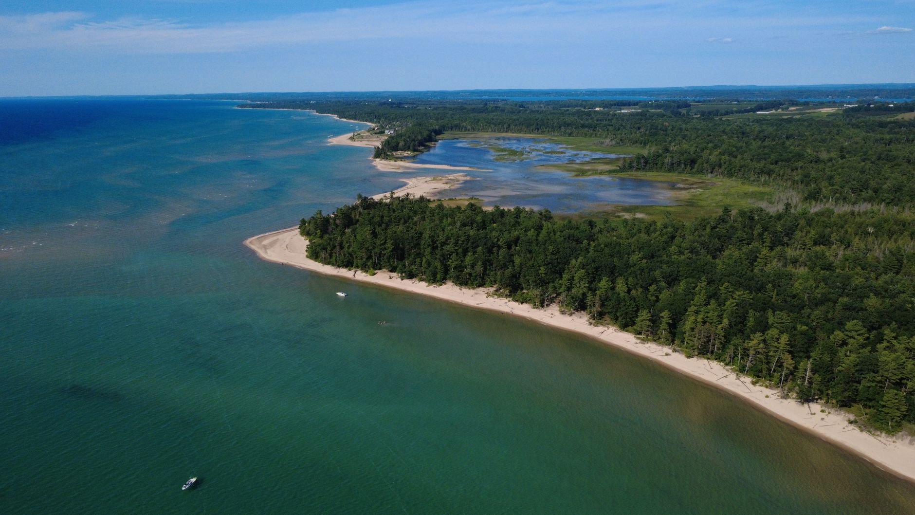 Drone shot of Michigan's coastal landscape with lush forests and clear waters in summer.